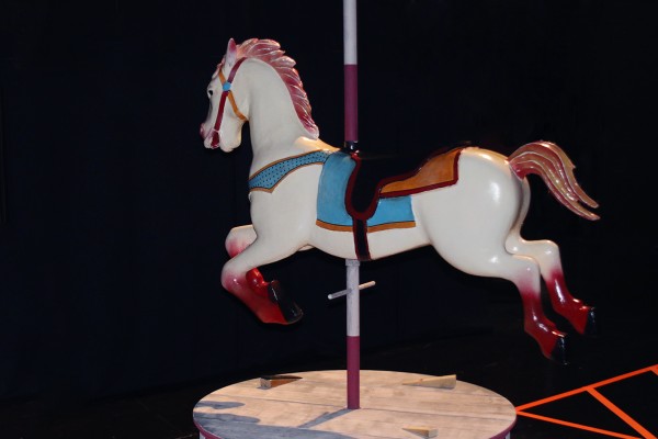 A profile of a white tivoli-horse with red feet and blue saddle